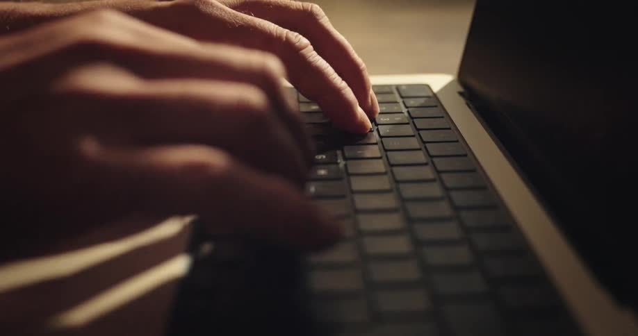 Mans fingers typing on the keyboard of a laptop computer