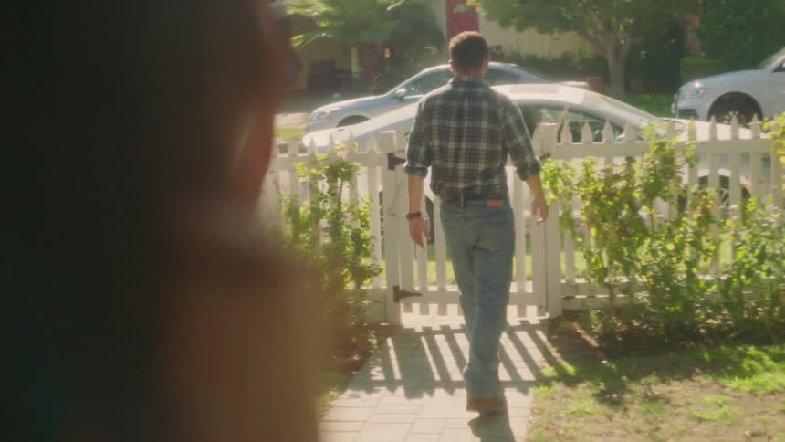 Man leaving front yard and walking out white picket fence on sunny day