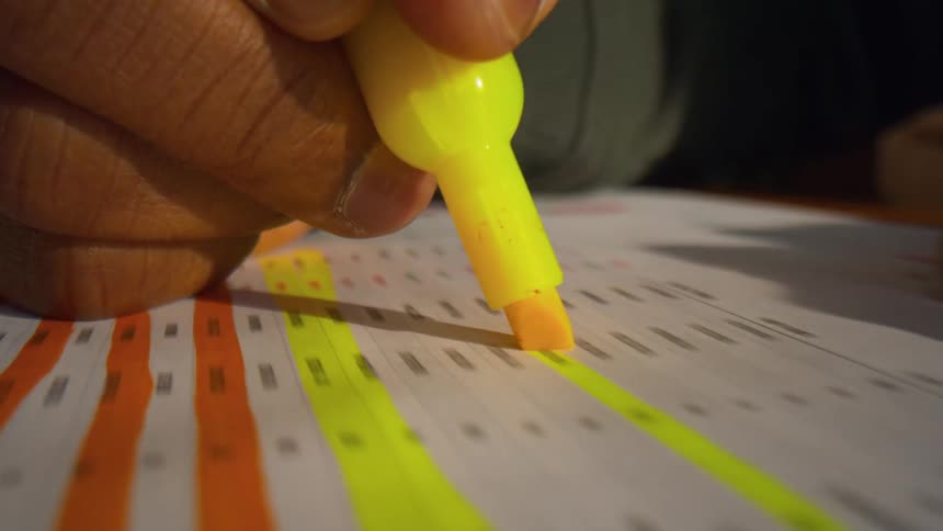 A person highlights a line on a paper spreadsheet with a yellow highlighter