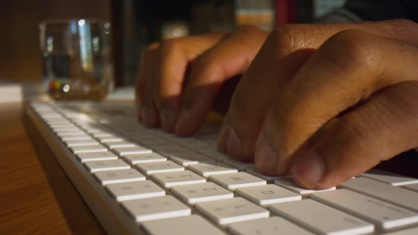 Hands typing on white keyboard with glass cup in the background on table