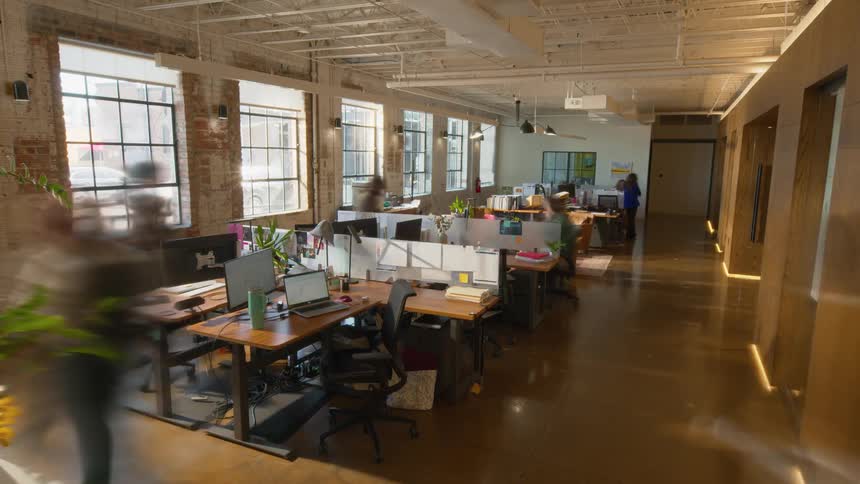 A wide angle view shows several people moving quickly through a modern office with desks and computers