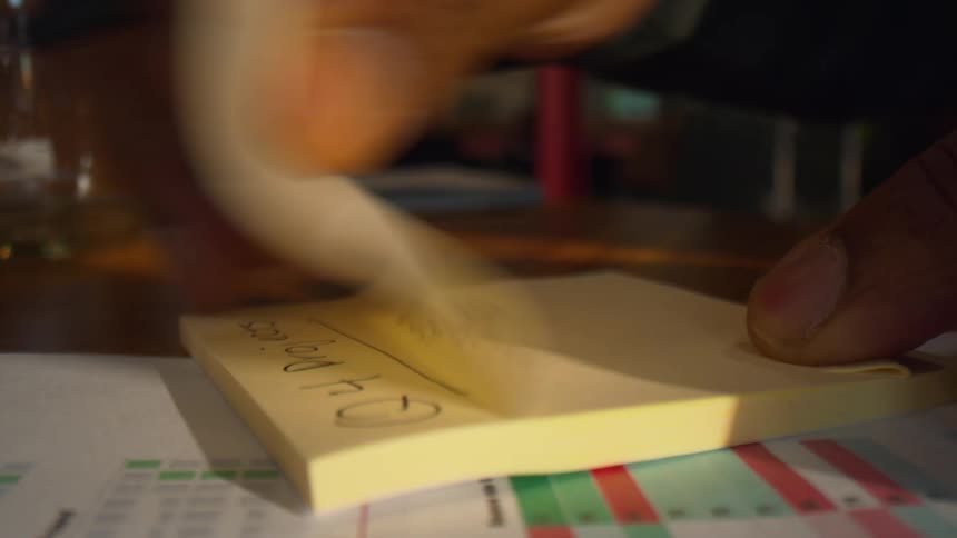 Hand turning page of notepad over documents with colored chart on table