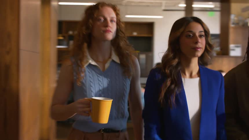 Three professionals walking through office one holding mug and another carrying folder