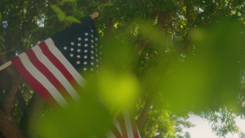 American flag seen before some trees while being taken down from a front porch
