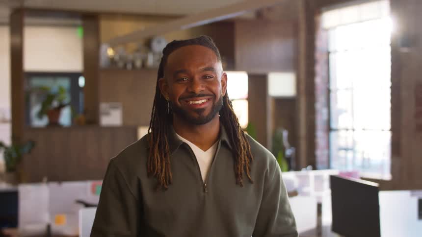 Man smiling with arms crossed in office with desks and windows in the background