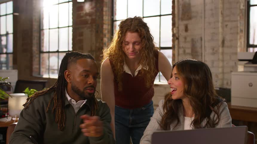 Three diverse colleagues collaborate around a laptop and documents in a modern office