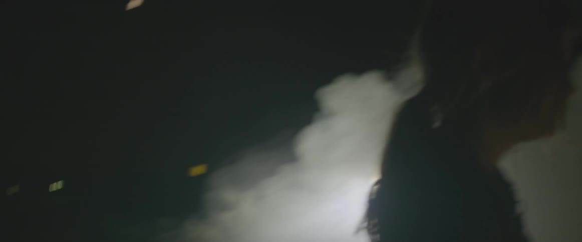 A woman walks outside in front of smoke and flashing lights