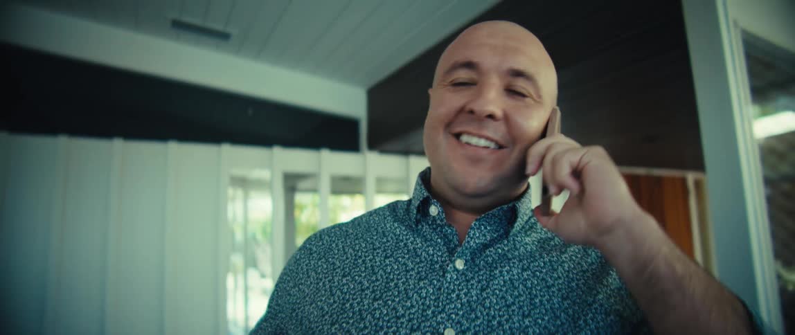 Man smiling while talking on phone indoors with glass doors in the background