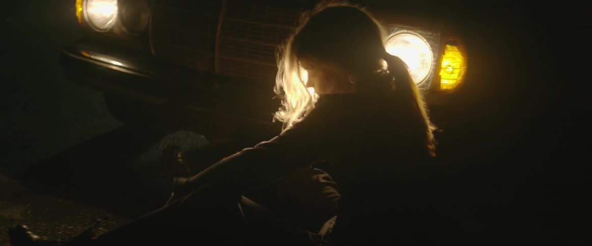 A woman dances in front of a car's headlights