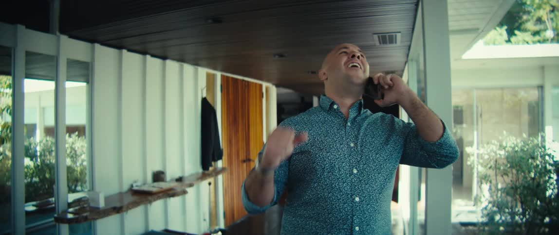A man answers a call on his phone then smiles and pumps his fists in the air