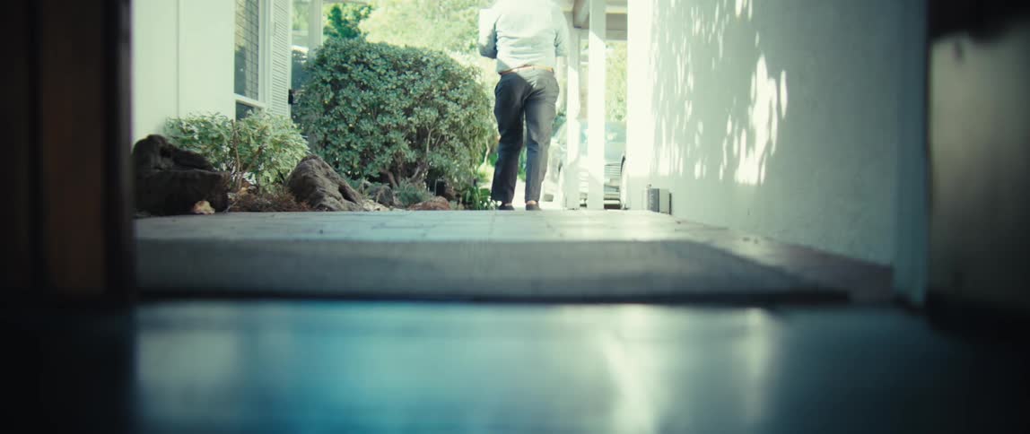A man wearing trousers and a shirt walks out of a building on a sunny day