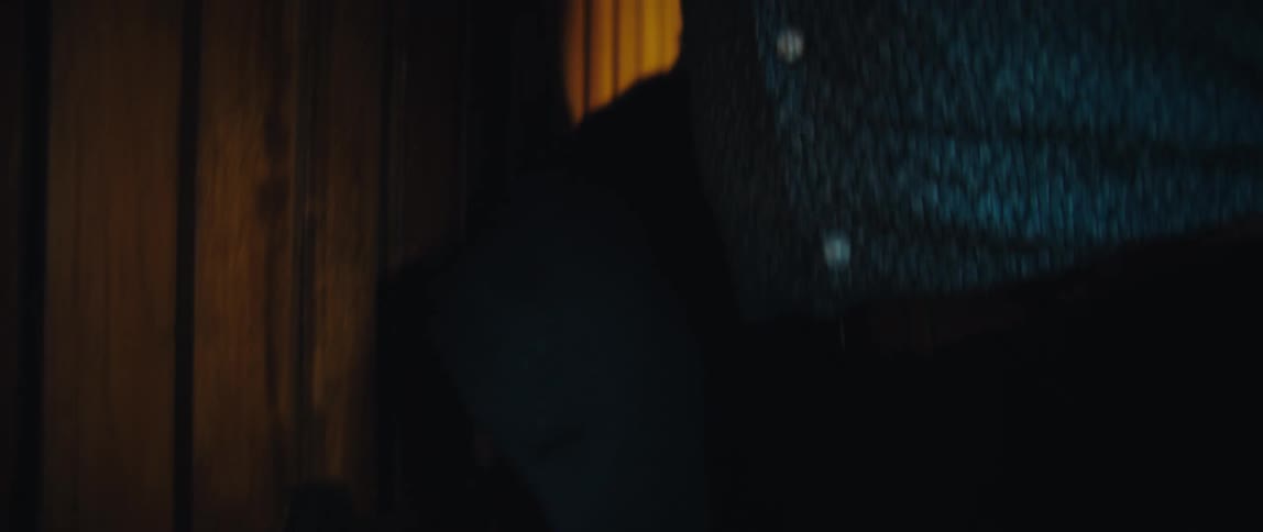 A man enters a room through a wooden door hangs his jacket on a hook and checks his smartphone