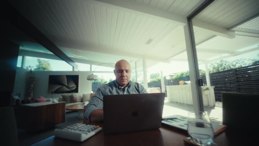 A man sitting at a table using a laptop in a house