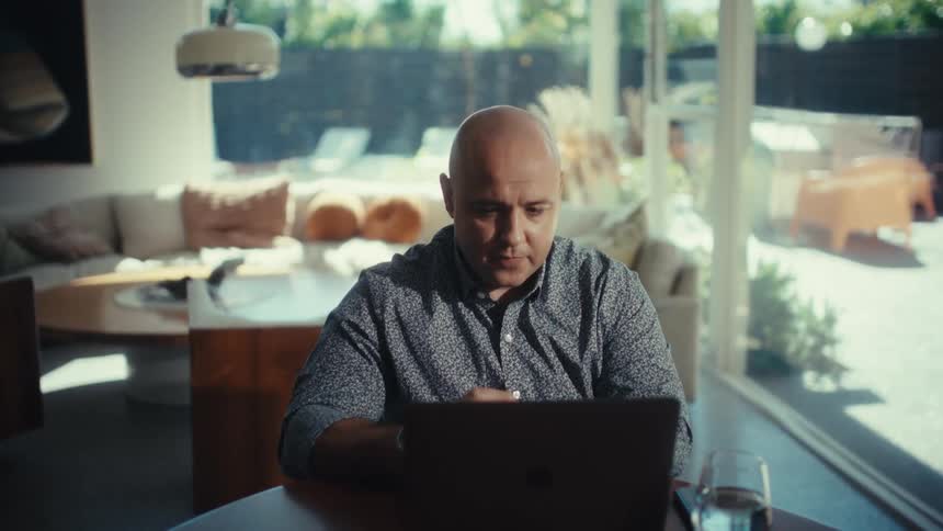 A man sitting at a table using a laptop in a room