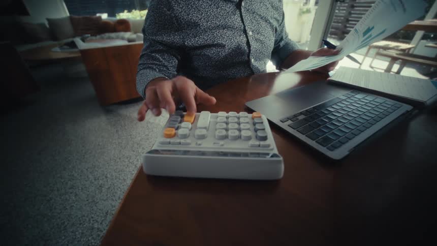 Man holds sheets with charts beside an open laptop on a table