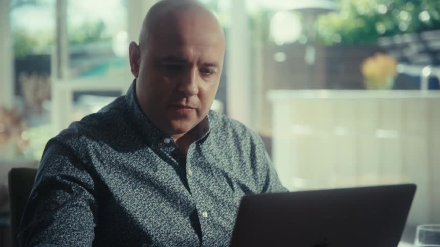A man sitting at a table using a laptop in a room