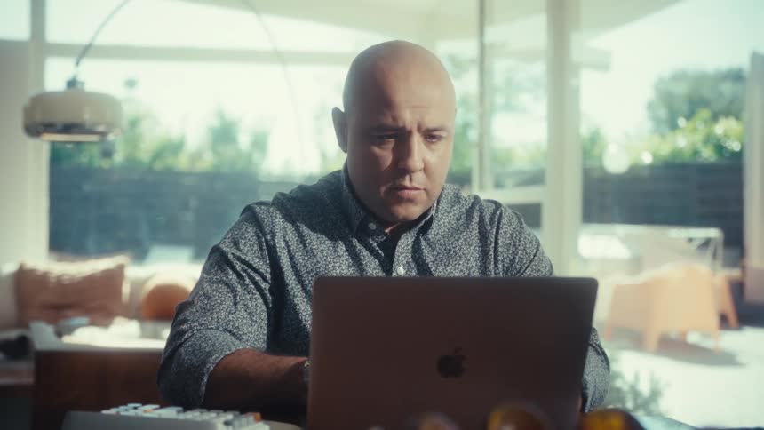 Man focused working on laptop at table with notebook and decorative object in the foreground