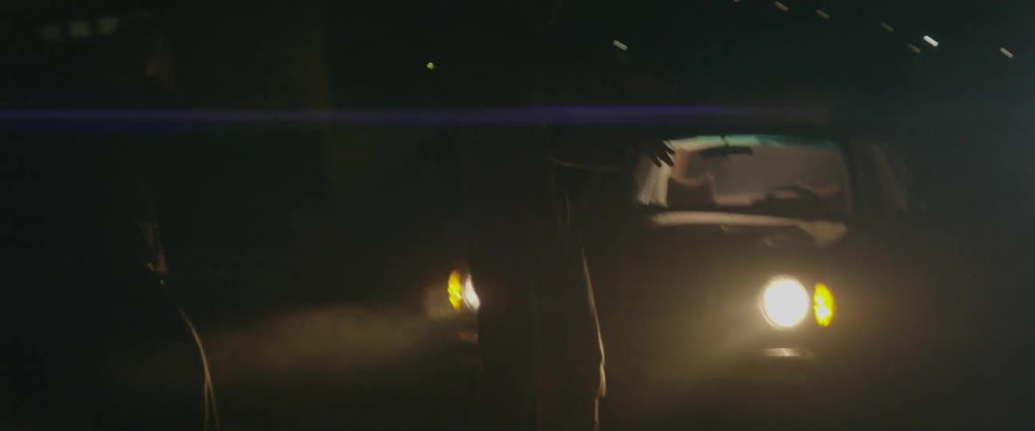 Two people dancing in front of car headlights