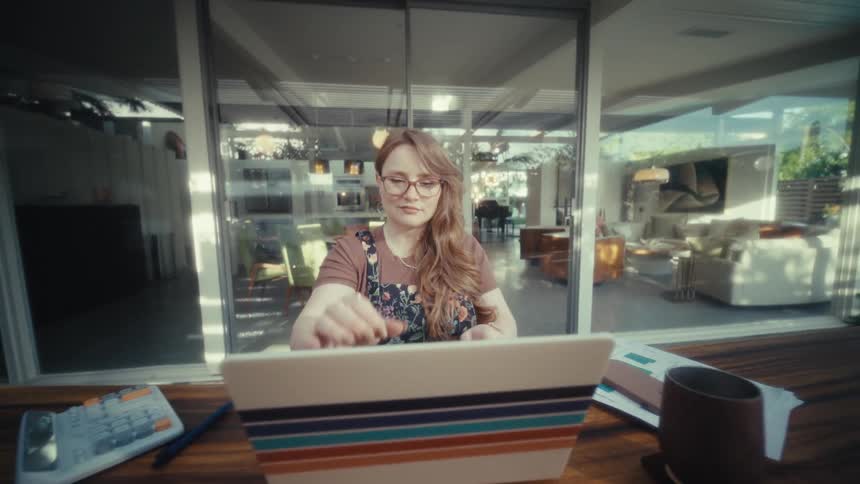 Woman wearing glasses opening stripedcover laptop on table in front of glass doors