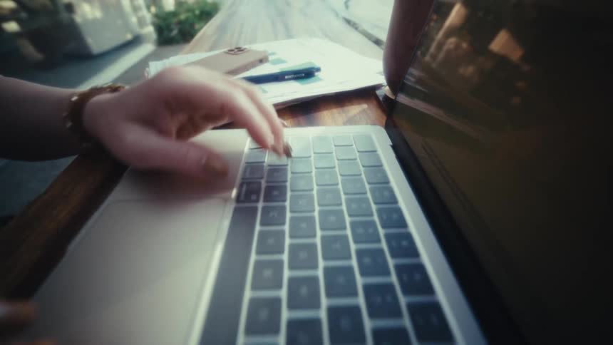 Hands typing on laptop on wooden table with notebook in the background