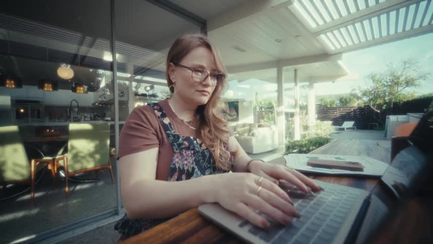 Woman wearing glasses opening stripedcover laptop on outdoor table with mug beside it