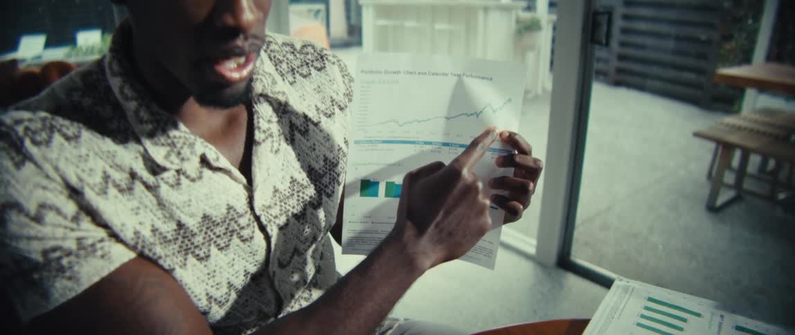 Man points to a chart on a sheet while holding a document near a table