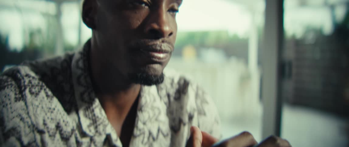 Man sitting indoors frowns with his hands clasped in front of him