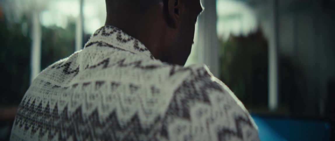 A young black man sits indoors typing on a computer keyboard at midday