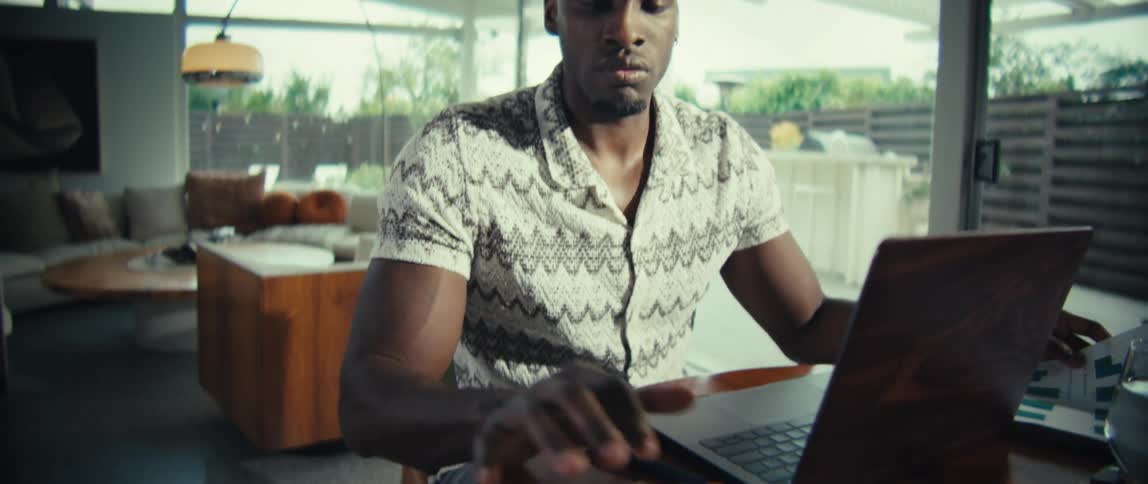 Man sitting at a table in front of a laptop computer holding a document and pressing keys on a calculator