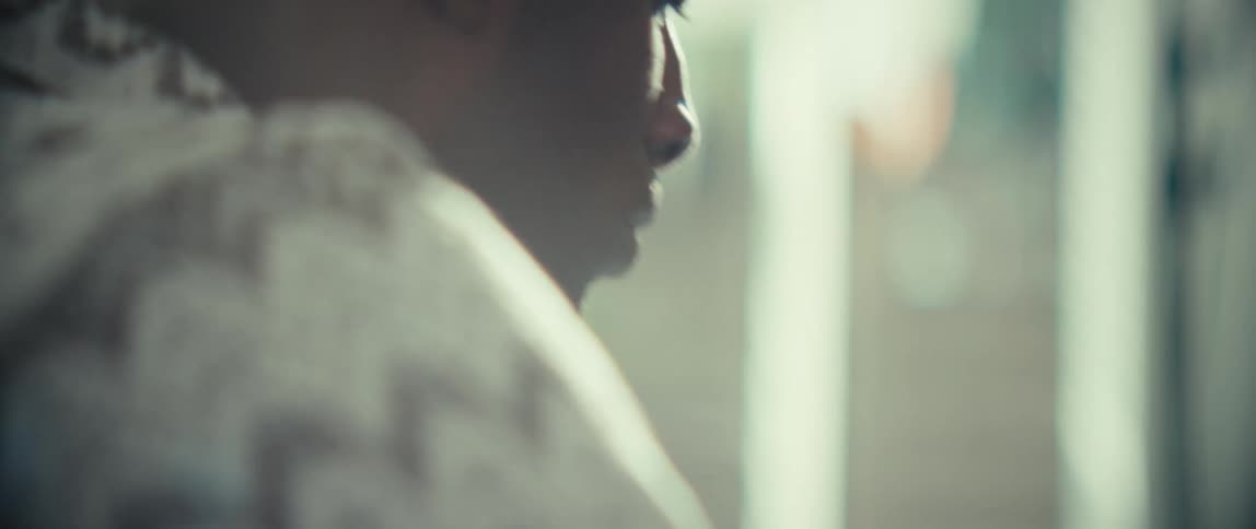 A black man is sitting at a desk typing on a laptop in a sunlit room