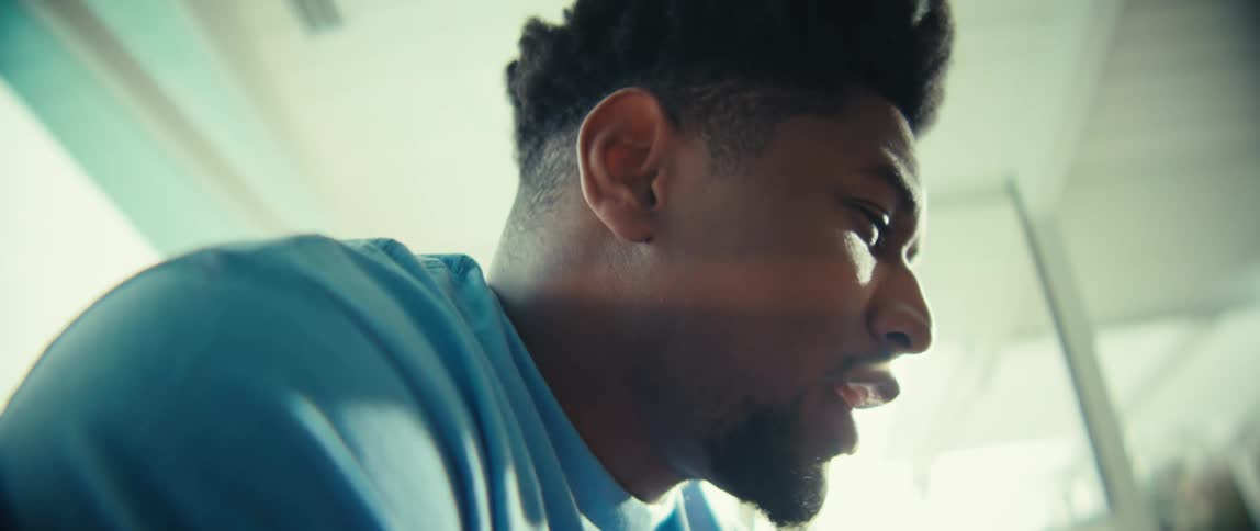 A black man from the shoulders up is talking smiling and shaking his head while looking forward in a sunlit room