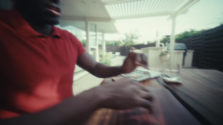 Hand closes a laptop on a wooden table in a covered outdoor area