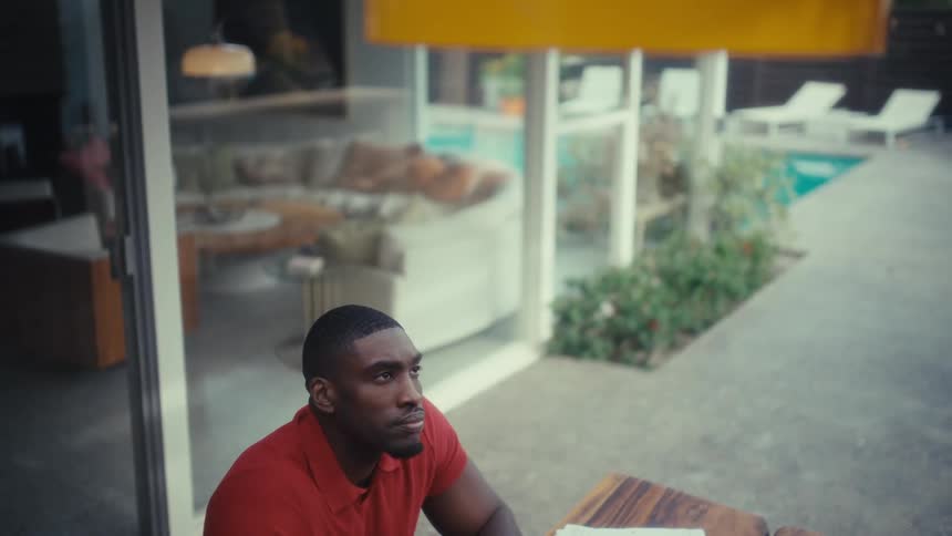 Man sitting outside his house at a table during the day looks up and smiles