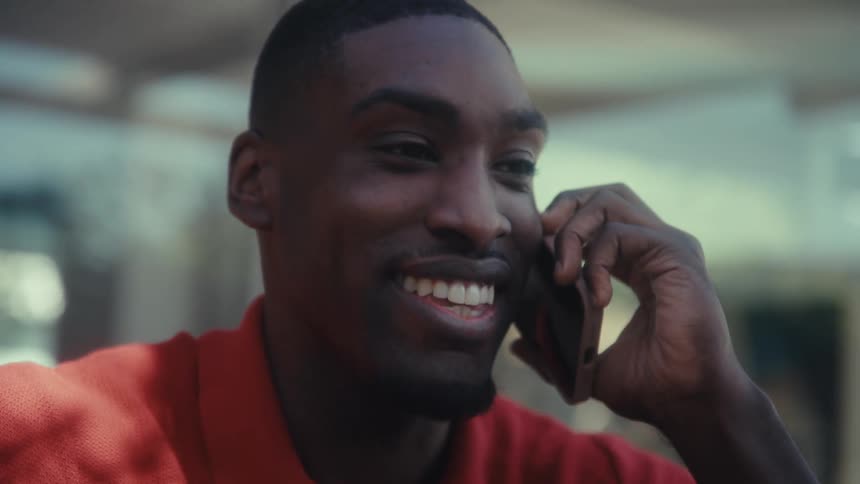Man smiles while talking on a mobile phone in a welllit indoor setting