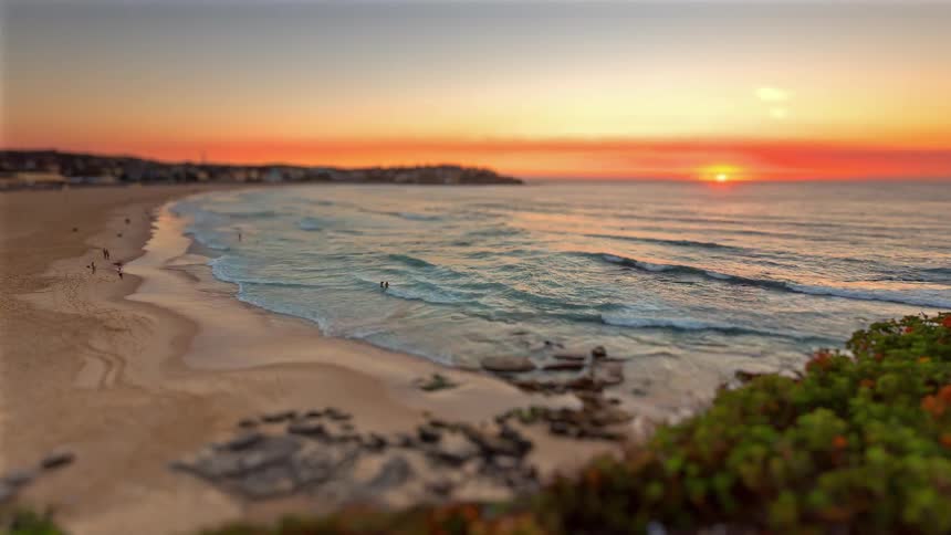 Beach with gentle waves and the sun setting on the horizon under an orange sky