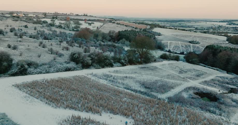 Landscape with slopes and hills covered in snow with sparse vegetation outdoors during dusk or dawn