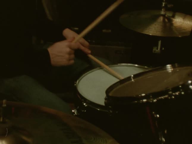 Young adult man wearing headphones playing drums in a room indoors