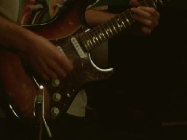 Young adult man wearing headphones playing an electric guitar in a room indoors