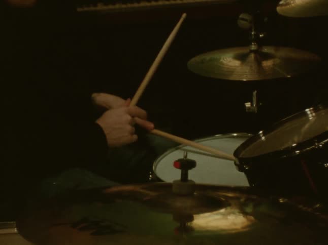 A persons arms and hands are seen playing drums in a dimly lit room