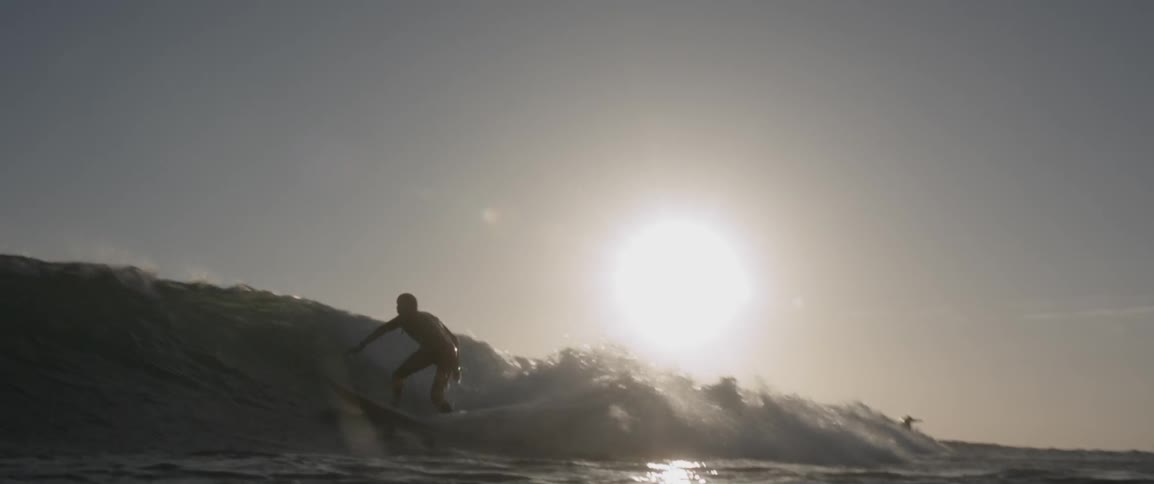 Man surfing a wave with bright sun behind him