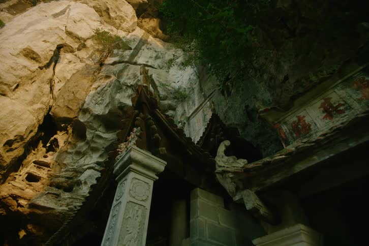An ancient temple structure with ornate stone pillars and carved details is built into the face of a rugged cliff