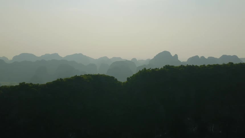 Layers of misty mountain ridges stretch across the horizon under a pale sky at dusk