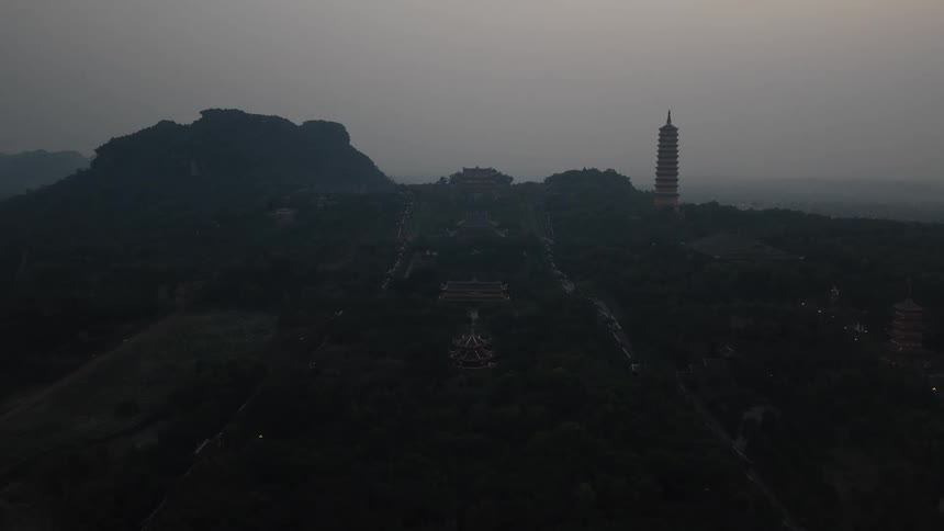 Asian pagoda tower stands tall on a mountain under a hazy sky with buildings on the mountainside
