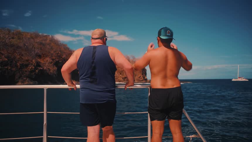 Two men are looking out off the side of their boat