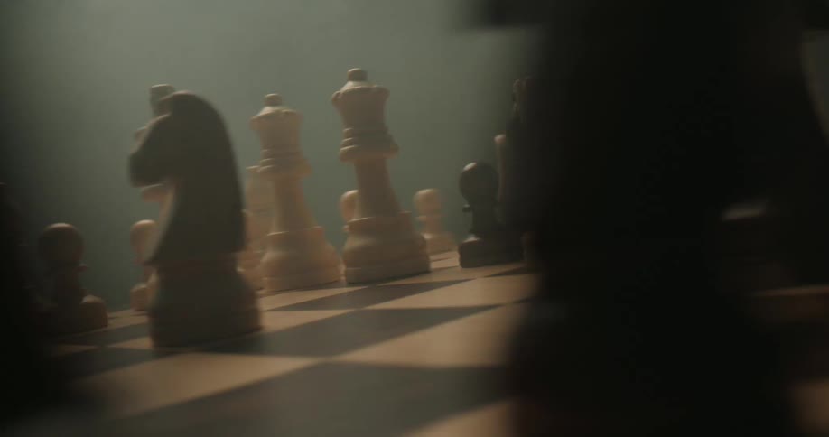 A close view shows various black and white wooden chess pieces standing on a game board while light smoke drifts through the air against a dark background