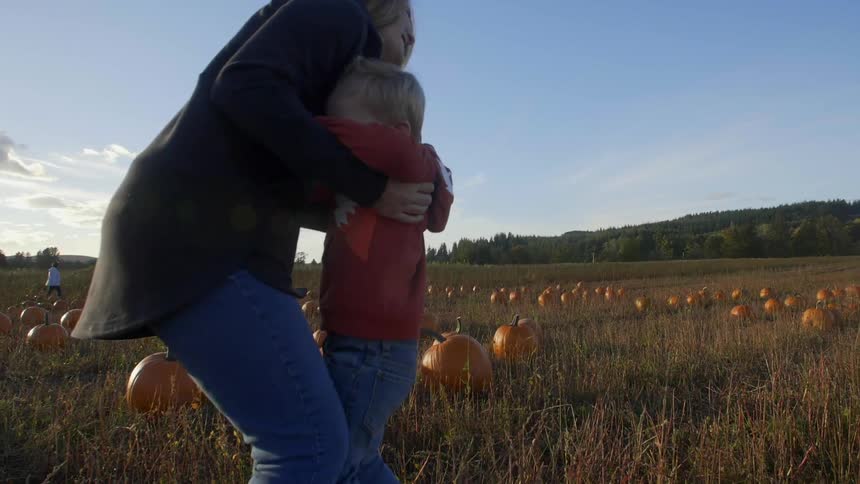Woman picks up little boy who is smiling and running to her in pumpkin patch