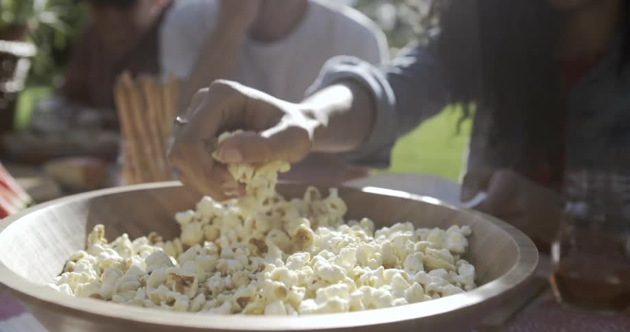 Person grabs a handful of popcorn out of a bowl and puts it on a place