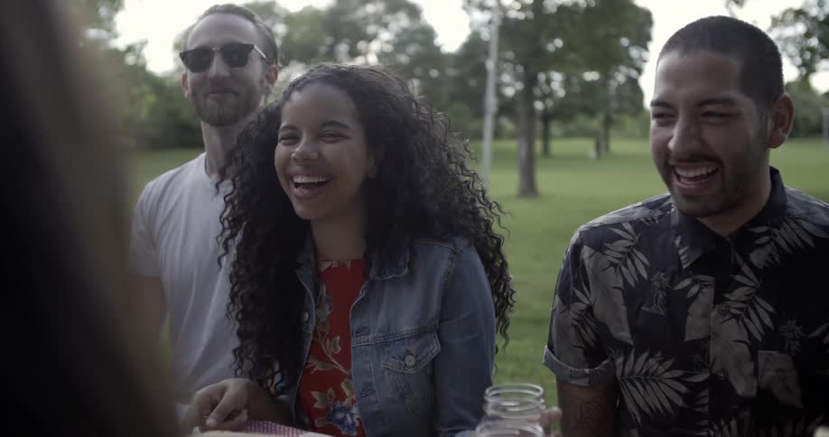 A group of people smile and laugh while eating at a picnic table
