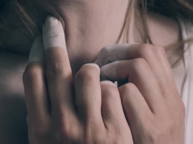 A close view shows the hands of a person with white powder on their fingers pressing against the skin of their neck