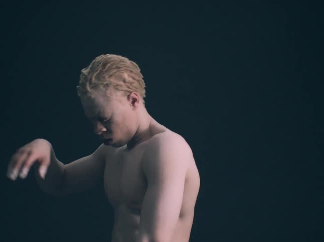 Shirtless albino black man dancing indoors